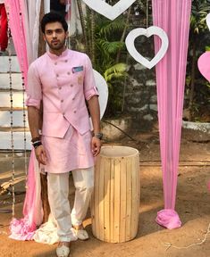 a man in a pink outfit standing next to a wooden barrel with flowers on it