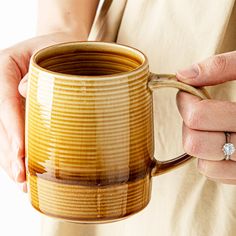 a woman holding a coffee mug with a diamond ring on her finger and wearing a tan dress