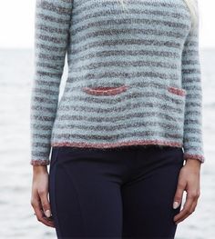 a woman standing in front of the ocean wearing a gray and black sweater with stripes