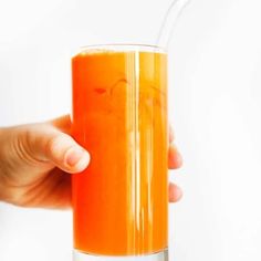 a person holding a glass with orange juice in it and a straw sticking out of the top