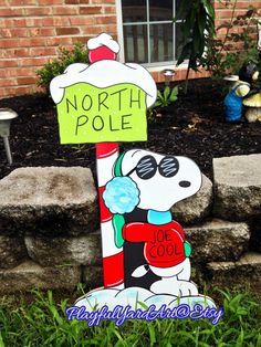 a wooden sign that says north pole with a snoopy dog holding a candy cane