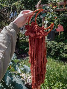 a person holding up a red piece of yarn hanging from a string in a garden