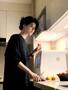 a woman standing in front of a kitchen counter preparing food on a cutting board next to an appliance