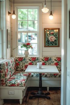 a corner table and bench in front of a window with flowers on the seat area