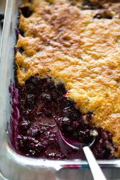 a blueberry cobbler in a metal pan with a serving spoon on the side