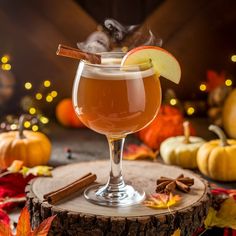 an apple cider sits on a tree stump surrounded by fall leaves and pumpkins