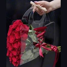 a bouquet of red roses in a clear plastic bag with ribbon tied around the handle