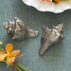 three seashells sitting on top of a table next to flowers and a plate