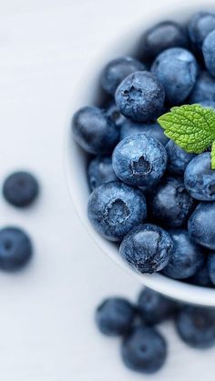 blueberries in a white bowl with a green leaf