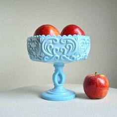 two apples sitting in a blue bowl next to an apple on a white tablecloth