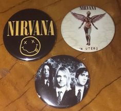 three button badges depicting nirvana, in utero and nirvana on wooden table with black background