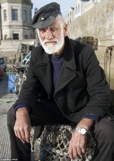 an old man sitting on top of a bench next to a fence and building in the background