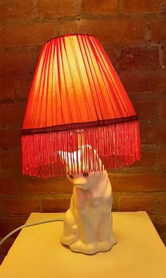 a white bear lamp sitting on top of a table next to a brick wall with a red shade