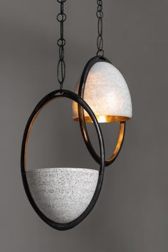 two circular lights hanging from chains on a gray wall, one light is white and the other is black