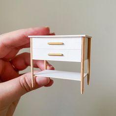 a miniature white drawer with gold handles is held up by a person's hand