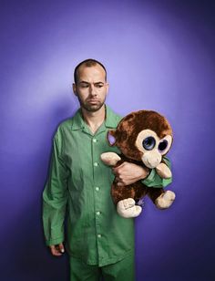 a man in pajamas holding a stuffed animal monkey on his chest and looking at the camera