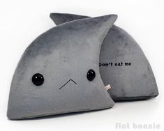 two gray pillows with black eyes and one has a shark's head on it