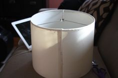 a white lamp shade sitting on top of a couch next to a laptop computer and pair of scissors