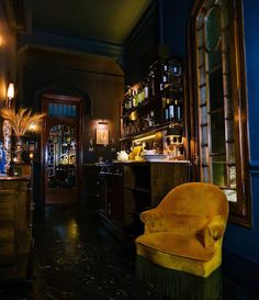 an old fashioned bar with yellow chairs and shelves full of liquor bottles on the wall