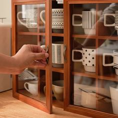 a person is opening the glass door of a cabinet filled with coffee cups and mugs