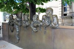 a group of bronze statues sitting on top of a metal wall next to a tree