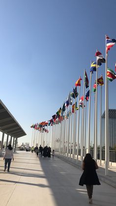 many flags are flying in the air near people walking on a sidewalk next to a building