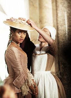 two women dressed in period clothing standing next to each other with hats on their heads