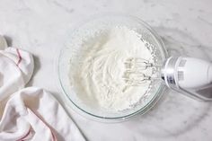 an electric mixer with whipped cream in it on a marble counter top next to a towel