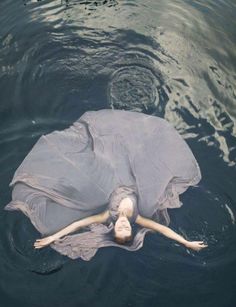 a woman floating in the water wearing a gray dress with her arms spread out and head down