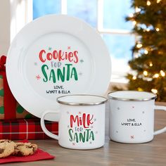 two white mugs sitting on top of a wooden table next to a christmas tree