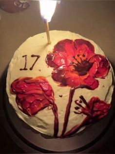 a birthday cake with white frosting and red flowers on it, lit by a single candle