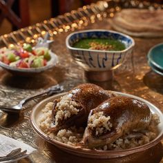 two chicken legs covered in rice sit on a plate next to bowls of vegetables and soup