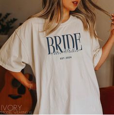 "Personalize your last name bride shirt with your new last name and custom just married year! This classy design is the perfect gift for a future wife / bride to be! **UNISEX T-SHIRTS- Run true to size. If wanting a more oversized look, selecting 1 or 2 sizes up is recommended. **CUSTOMIZATION-If you would like this design in a different color or on a different item (t-shirt, sweatshirt, tank top, bag, hat, etc.)-please message us and we will do our very best to get it made for you. Placing an o Bride And Groom T Shirts, White Bridal T-shirt With Short Sleeves, Customizable Short Sleeve Tops For Wedding, Customizable Short Sleeve Wedding Tops, Custom Name White Crew Neck T-shirt, White Short Sleeve T-shirt With Custom Name, White Crew Neck T-shirt With Custom Name, Custom Text Short Sleeve Tops For Wedding, White Custom Text T-shirt For Weddings