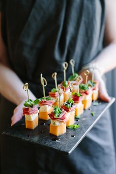 small appetizers are arranged on a black platter with toothpicks and garnishes