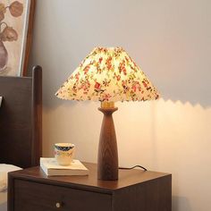 a lamp that is sitting on top of a night stand next to a book and cup