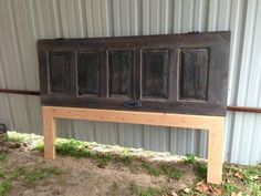 an old wooden bench sitting in front of a metal building with four panes on it