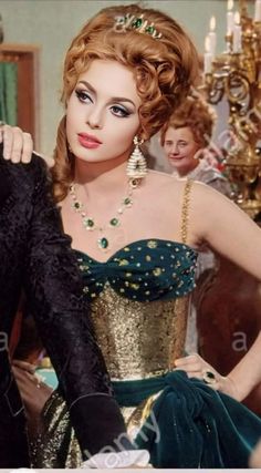 a woman in a green and gold dress is holding onto a black jacket with her hands