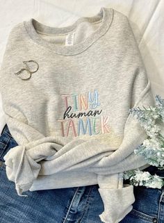 a sweater with the words tiny human tamer on it next to some blue jeans