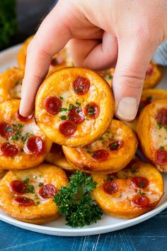 a plate full of mini pizzas with cheese and pepperoni on them, being held by a person's hand