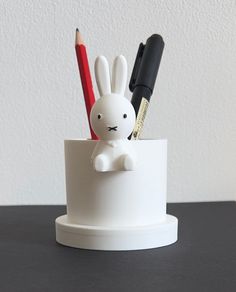 a small white rabbit sitting inside of a cup filled with pens and pencils on top of a table