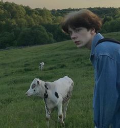 a young man standing next to a cow in a field