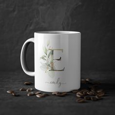 a white coffee mug with the letter e on it surrounded by coffee beans and steam