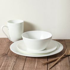 a white cup and saucer sitting on top of a wooden table next to a fork