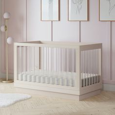 a white crib in a pink room with three pictures on the wall and floor