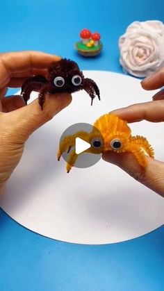 two hands are holding an orange crab and another hand is holding a yellow crab with googly eyes