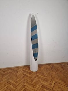 a white vase with a blue and grey striped surfboard in it on a wooden floor