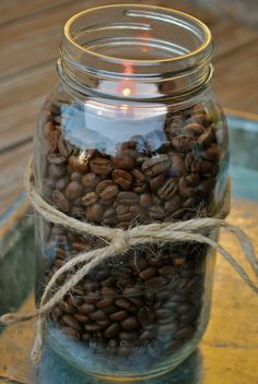 a jar filled with coffee beans sitting on top of a wooden table next to a lit candle