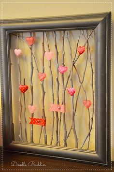 a frame with hearts hanging from it and some branches attached to the wall behind it