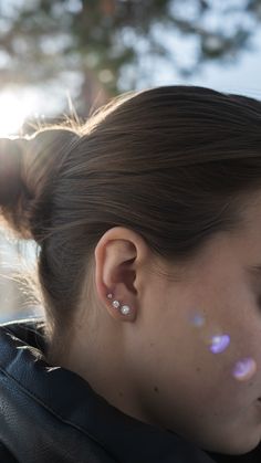 a young woman with ear piercings looking off into the distance, wearing a black leather jacket