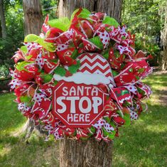 a red and white wreath that says santa stop here on the side of a tree